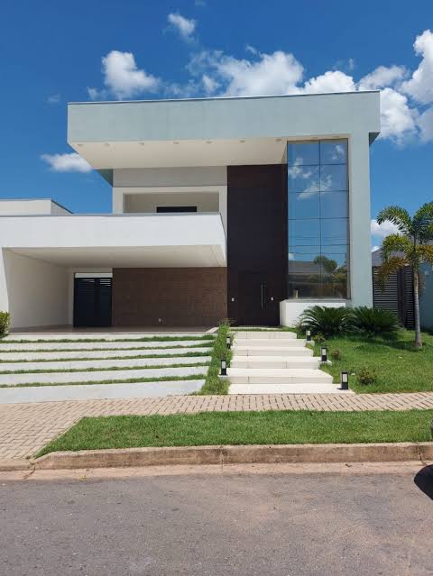 Modern white two-story house with dark brown accents, reflective windows, lawn, and driveway under a blue sky.
